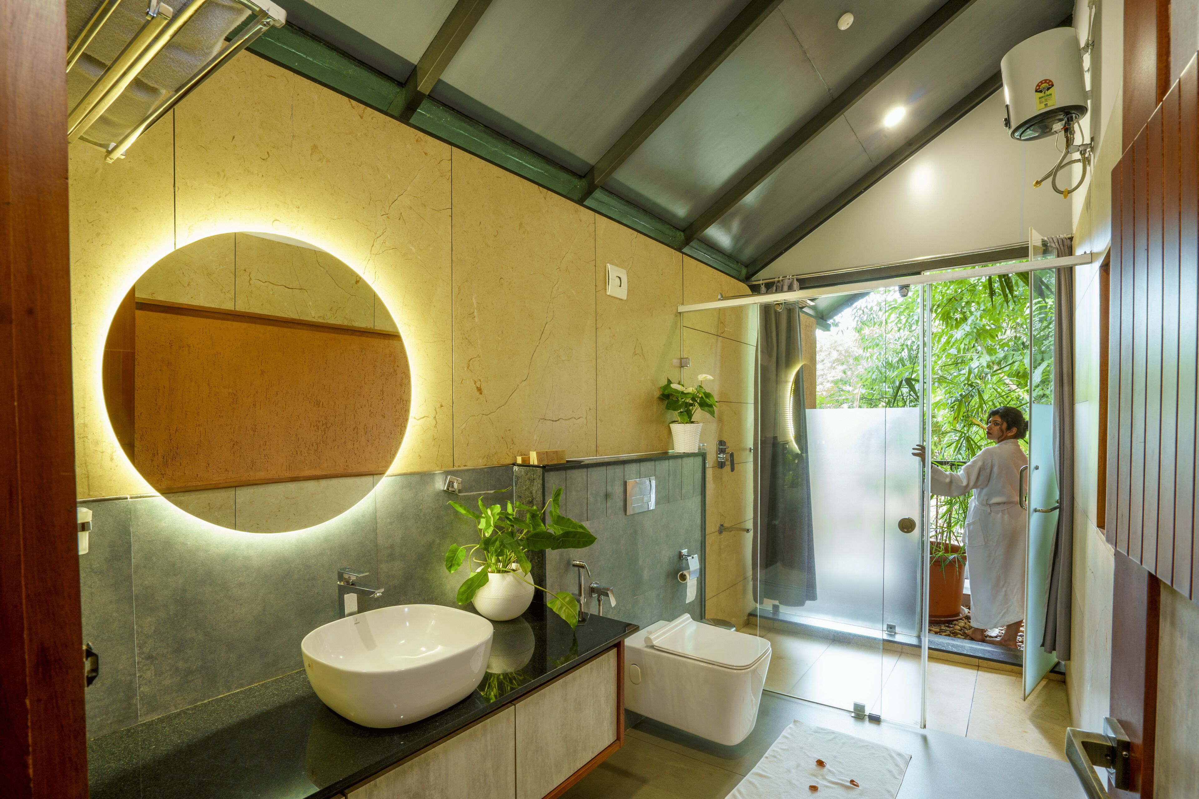 Une salle de bain moderne avec un grand miroir rond, un lavabo blanc et une cabine de douche en verre.