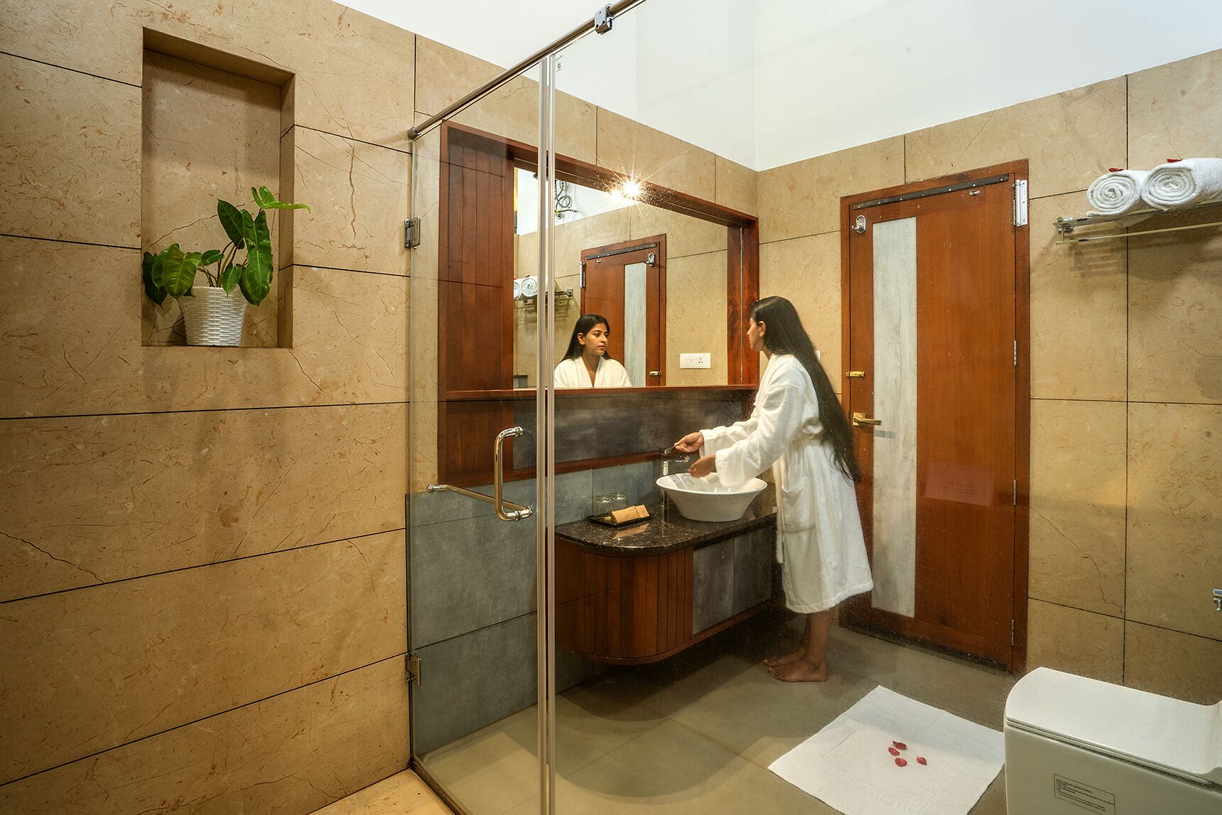 Un baño moderno con cabina de ducha de vidrio, un lavamanos con encimera de mármol y un mueble de tocador de madera.
