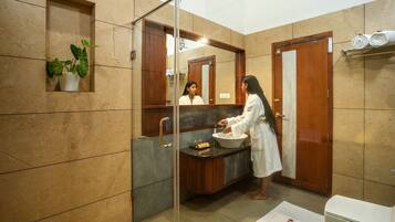 Un baño moderno con cabina de ducha de vidrio, un lavamanos con encimera de mármol y un mueble de tocador de madera.