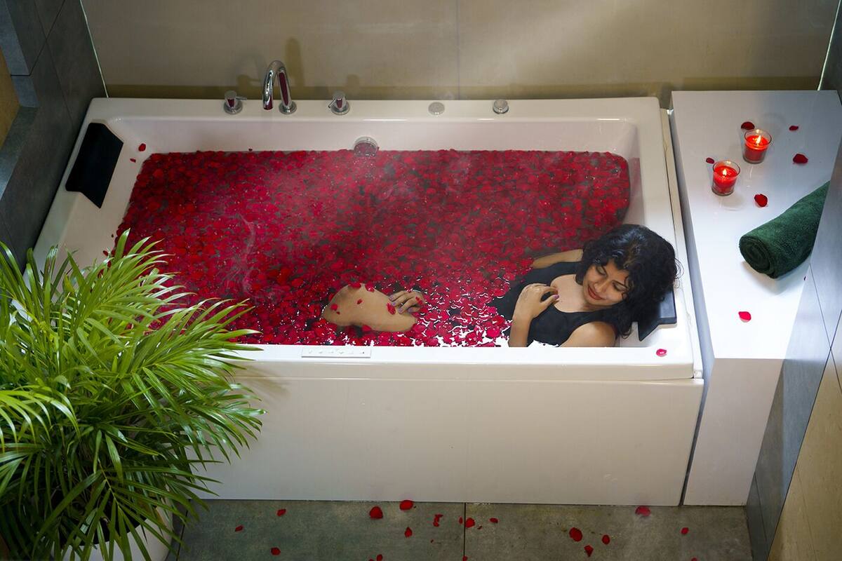 A bathtub filled with red rose petals, a green plant, and a towel on the side.