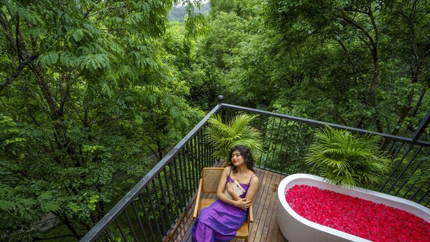 A woman sitting on a wooden deck with a railing, surrounded by lush greenery. - Crystal Kuruva Nature Resort & Spa (Sulthan Bathery)