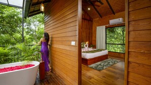 A wooden cabin with a large bathtub filled with red flowers, a bed with a green rug, and a window overlooking greenery. - Crystal Kuruva Nature Resort & Spa (Sulthan Bathery)
