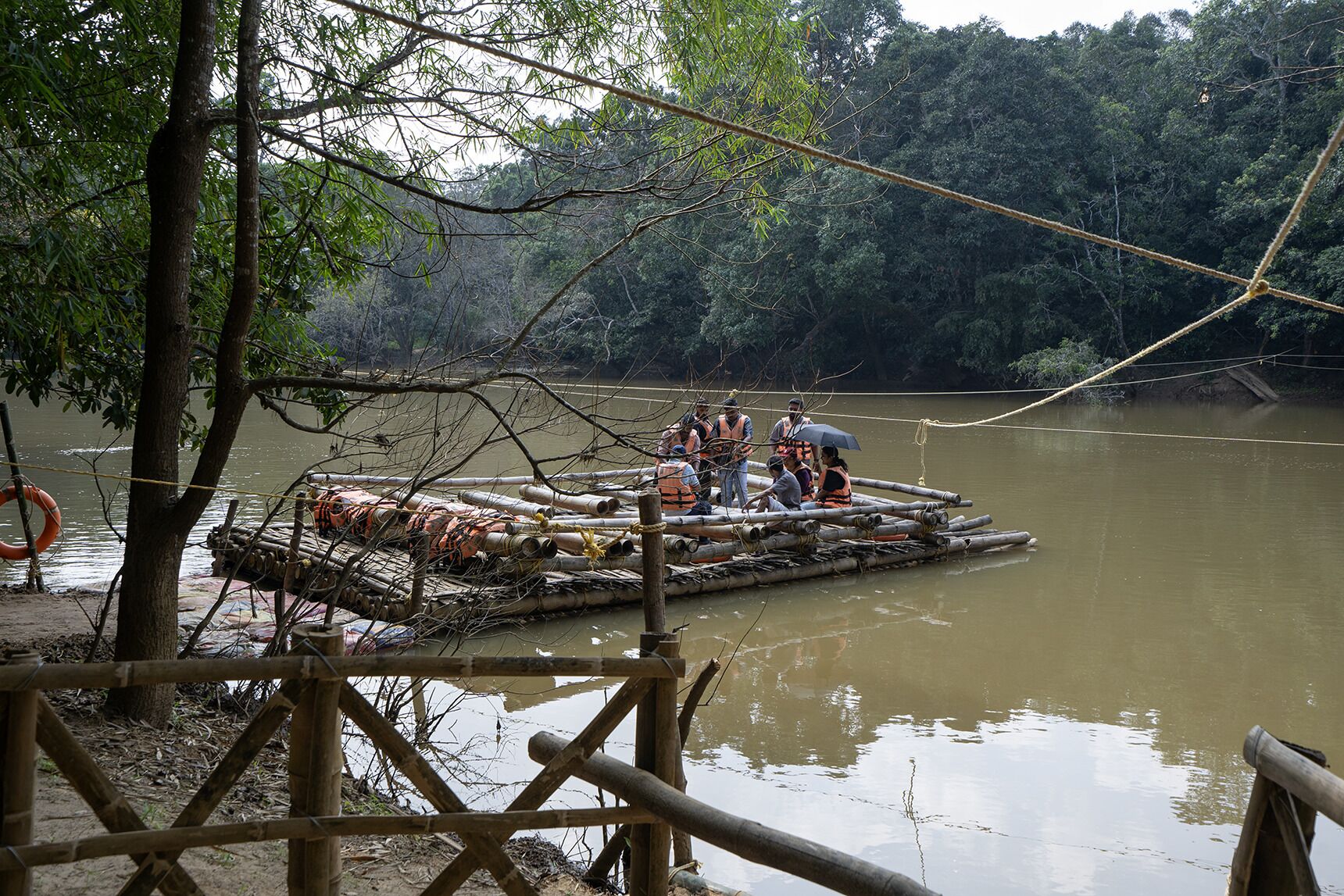 Een bamboevlot met mensen, omgeven door een bebost gebied en een rustige rivier.