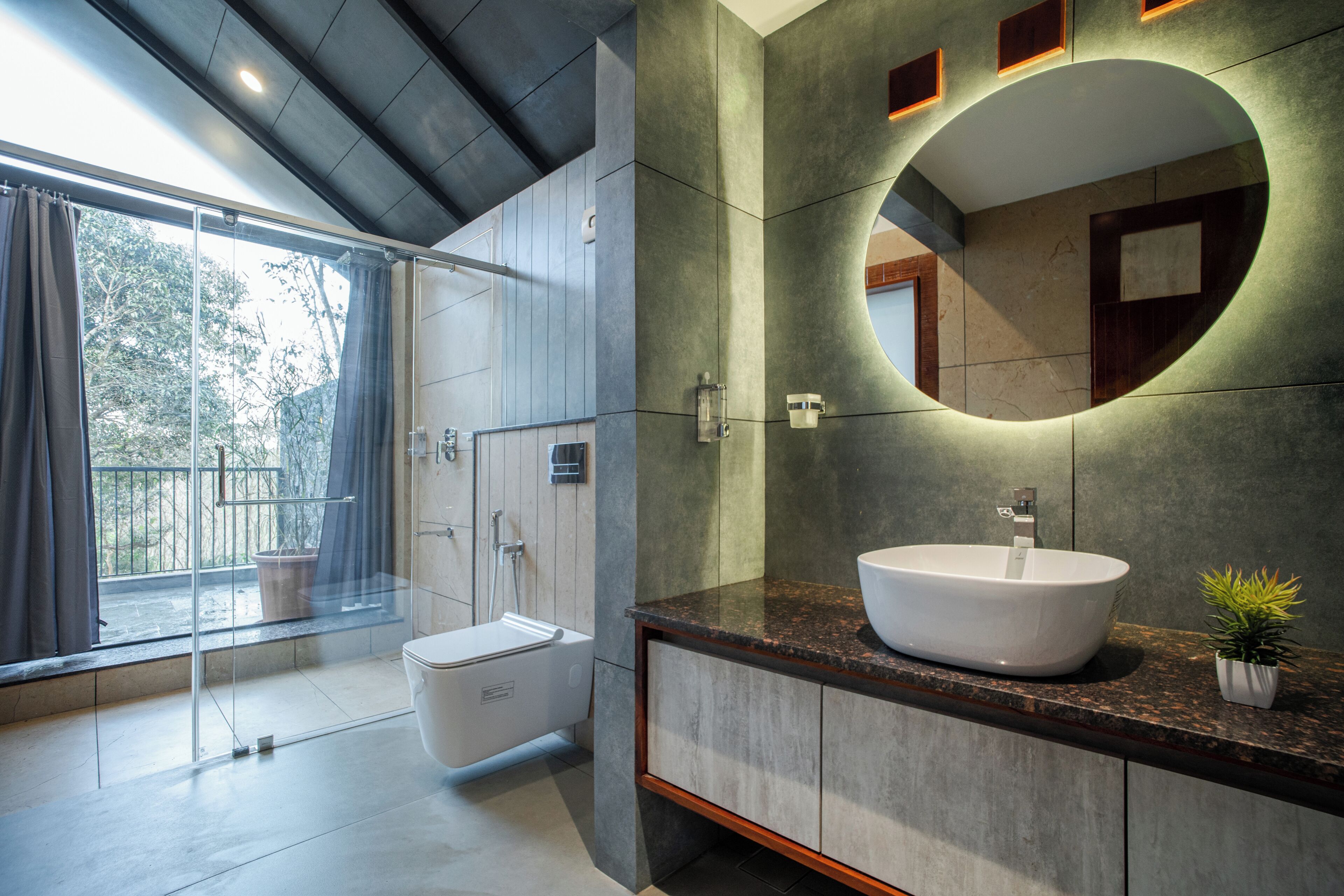Un baño moderno con un ventanal grande, una bañera, un lavamanos con espejo y una planta en maceta.