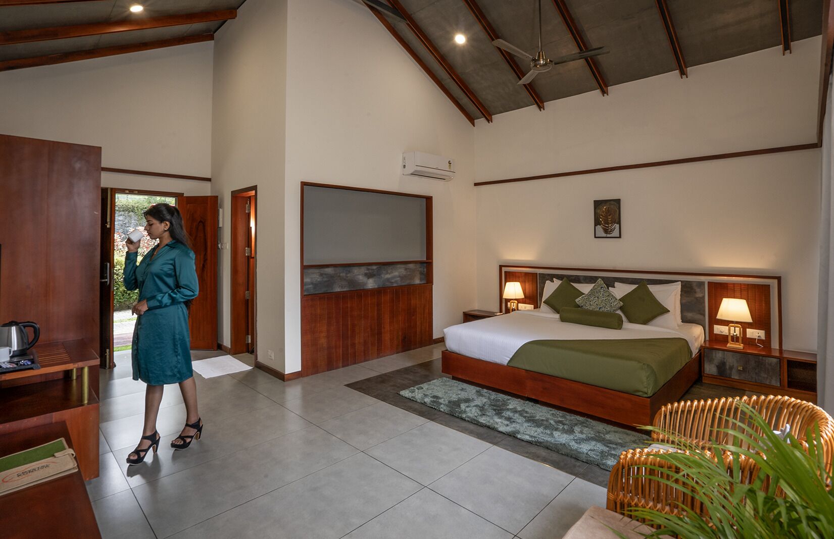 A hotel room with a bed, bedside lamps, a wooden headboard, a large mirror, and a view of the outdoors.