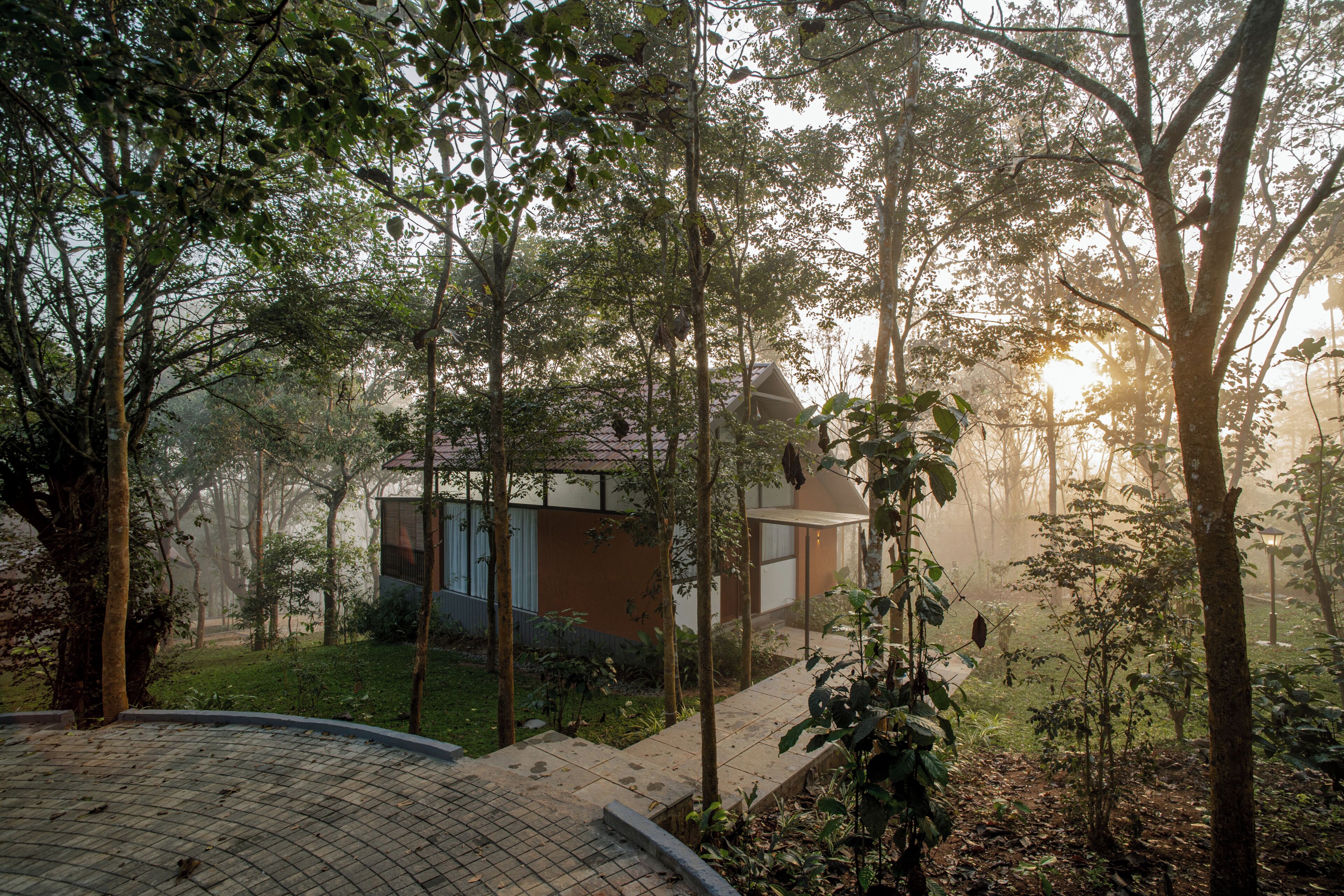 Una cabaña apartada rodeada de un bosque frondoso, con un camino pavimentado que lleva a la entrada.