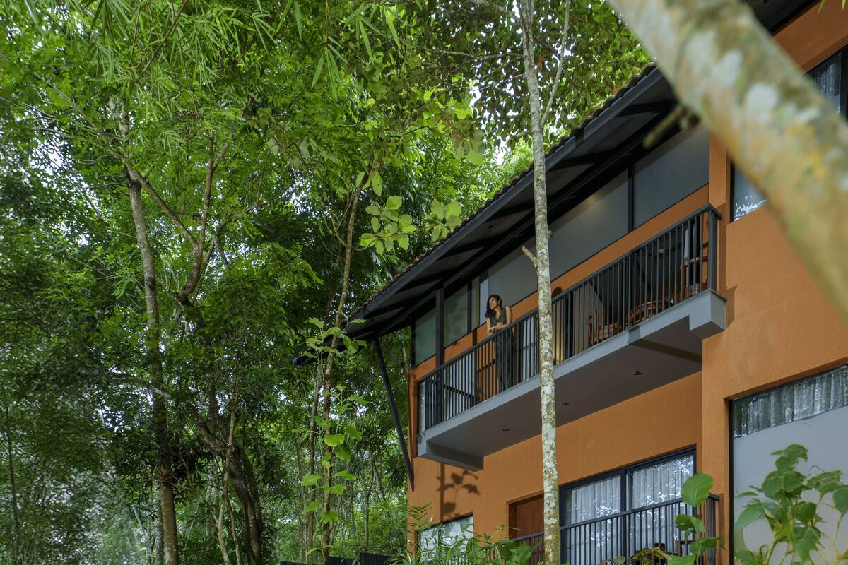 A multi-story building with balconies surrounded by dense green foliage.