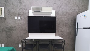Una cucina moderna con un piano di lavoro bianco, sedie nere, un frigorifero bianco e una televisione a schermo piatto montata sopra il bancone.