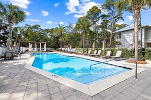 Relax by the serene pool surrounded by lush greenery and palm trees, with lounge chairs and umbrellas for a comfortable stay.