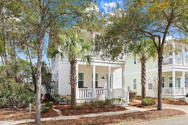 Situated on a paved driveway, this two-story home features a spacious porch and a balcony above, surrounded by mature trees.