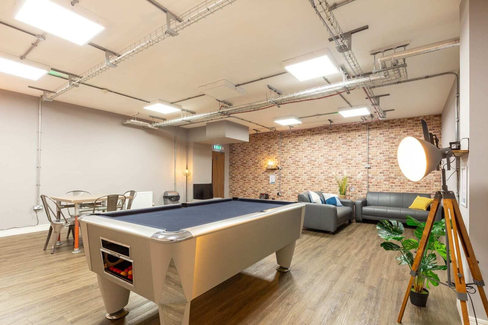 Une table de billard dans une pièce avec un mur en briques, un canapé et une plante en pot.