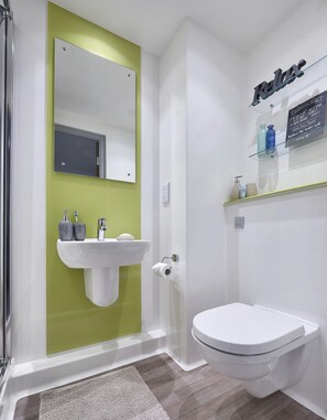 A bathroom with a white sink, a toilet, a mirror, and a shelf with toiletries.