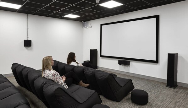 A modern home theater room with black sofas, a large screen, and speakers. - The Foundry (Leeds)
