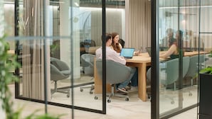 Un espacio de oficina con paneles de vidrio, mobiliario moderno y un diseño limpio y minimalista.