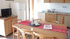 A compact kitchen with a dining area, a refrigerator, a stove, and a television. - Great Flat Next to the sea in Bibione (San Michele al Tagliamento)
