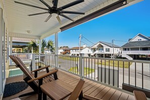 A covered outdoor area with wooden benches and a ceiling fan, overlooking a residential street with houses. - New Pool! Pet friendly. Perfect 4BR 3BA home. Sleeps 10. Short walk to beach. (North Myrtle Beach)
