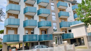 Un edificio residencial de varios pisos con balcones, un estacionamiento y una entrada portonada.
