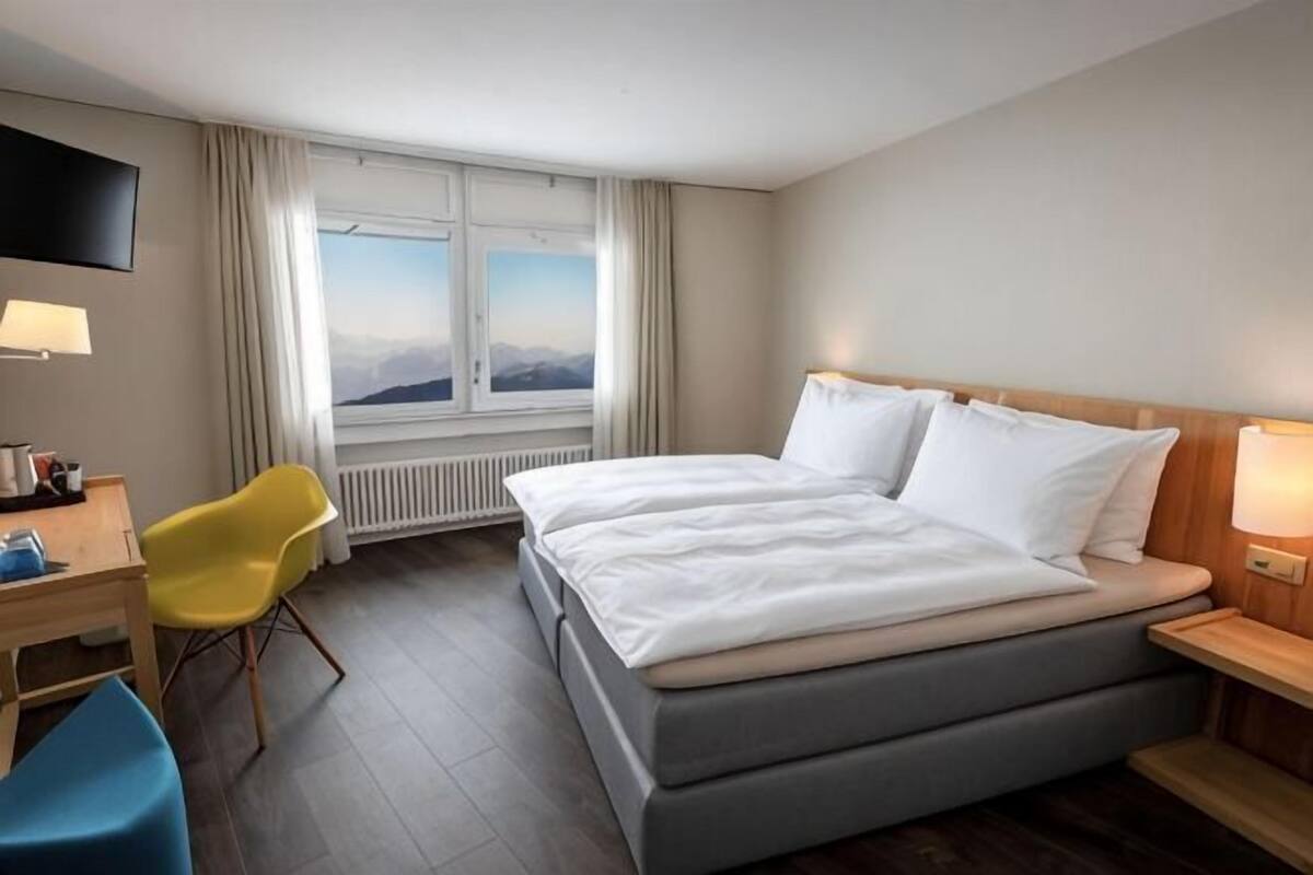 A hotel room with a bed, a desk, a chair, a TV, and a window with a view.
