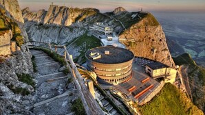 A hotel with a circular building structure, a staircase leading up to it, and a view of the surrounding mountainous landscape. - Hotel Bellevue (Alpnach)