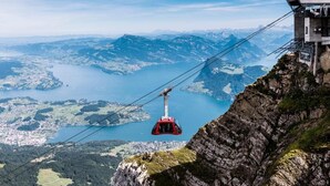 A cable car system with a red gondola, a mountainous landscape, and a lake below. - Hotel Bellevue (Alpnach)