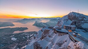 A snow-covered mountain with a lake and a building with a circular design. - Hotel Bellevue (Alpnach)