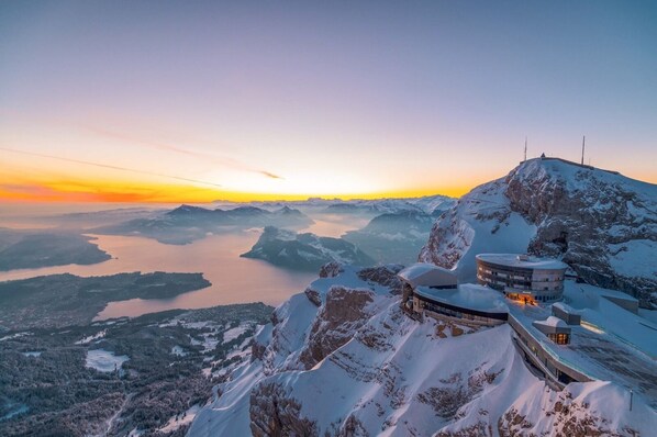 A snow-covered mountain with a lake and a building with a circular design. - Hotel Bellevue (Alpnach)