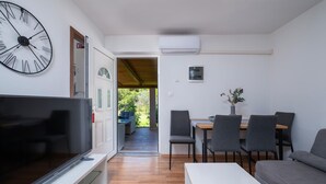 A modern living room with a flat-screen TV, a dining area with a table and chairs, and a large clock on the wall. - 2 bedroom nice home in Pula (Pula)