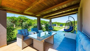 A covered outdoor seating area with wicker furniture, a glass-top table, and hanging chairs. - 2 bedroom nice home in Pula (Pula)