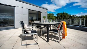A modern outdoor patio with a dining table and chairs, a sliding glass door leading to an interior space, and a metal railing along the edge. - For Students Only Stepney Yard in Newcastle (Newcastle-upon-Tyne)