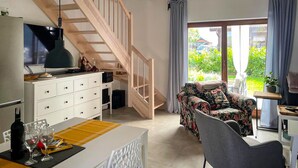 Ein geräumiger Wohnbereich mit einer Holztreppe, einem Esstisch mit Stühlen, einer Couch und Blick ins Grüne.