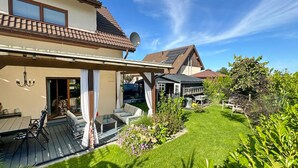 Ein Haus mit überdachter Terrasse, Rasen und Garten.