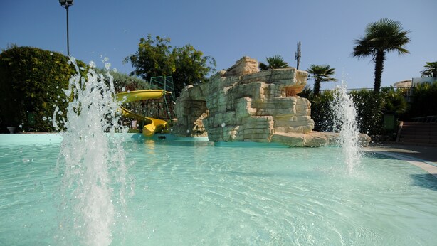 A water park with a clear pool, water slides, and a rocky structure. - Happy Camp in Camping Riccione (Riccione)