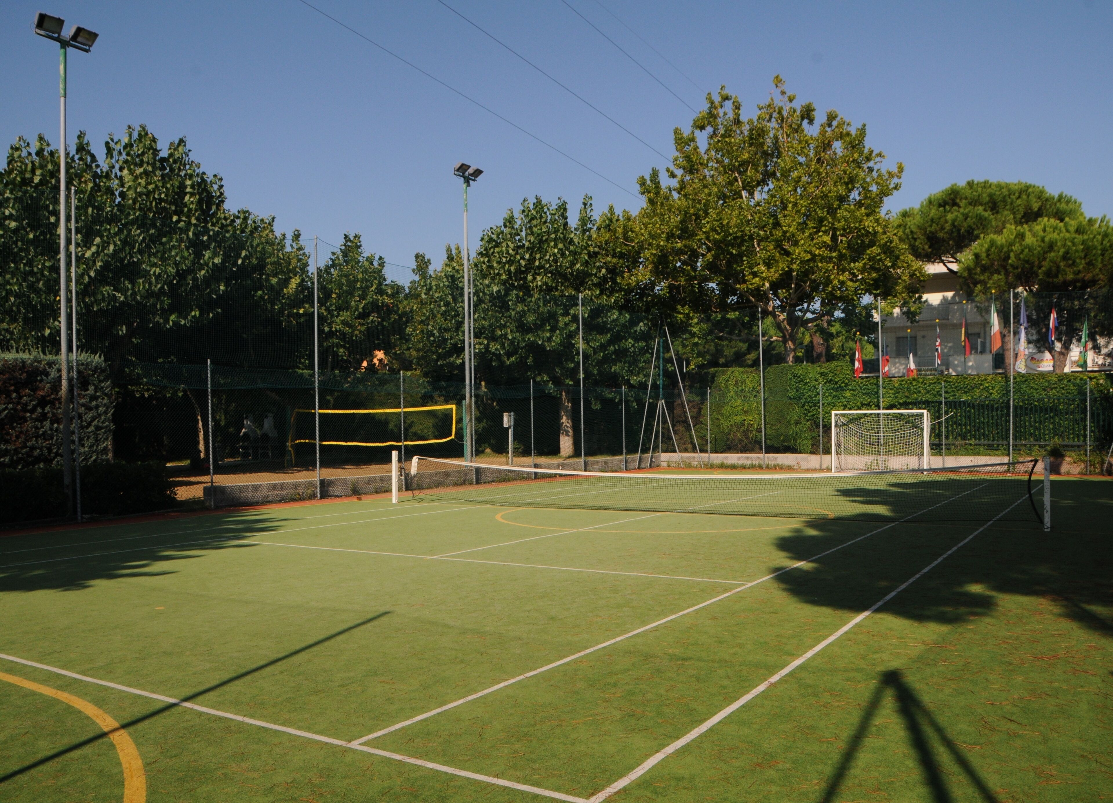 Un court de tennis avec un filet, entouré d’arbres et de drapeaux.