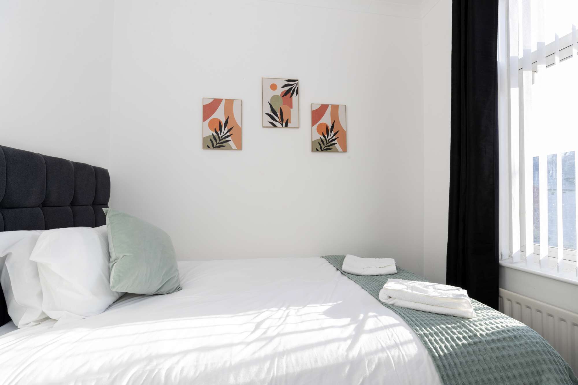 A hotel room with a bed, a window with curtains, and three wall-mounted artworks.