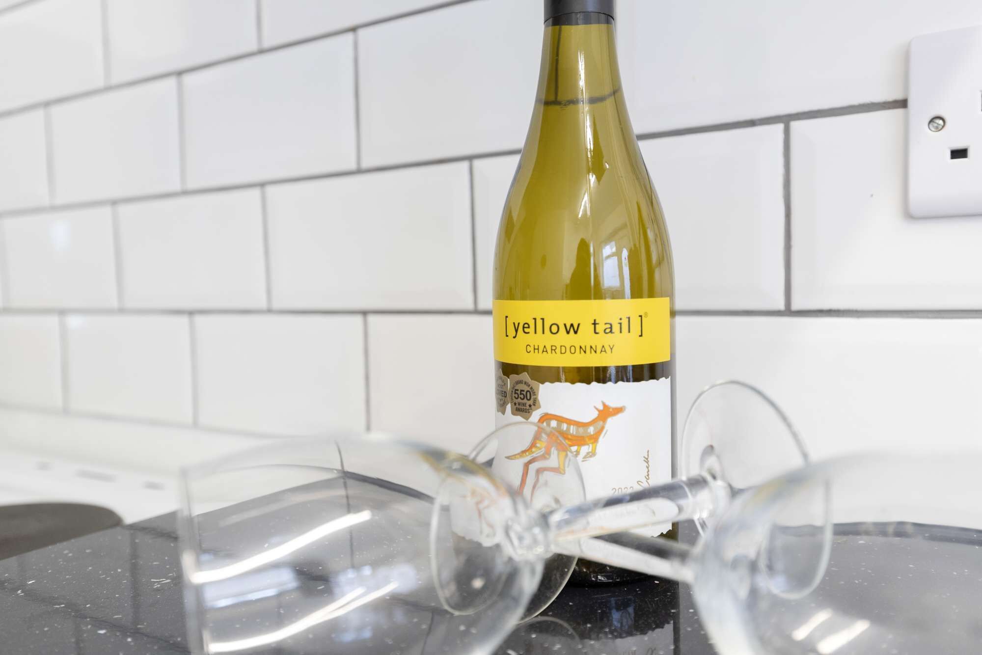 Une bouteille de Chardonnay [yellow tail] posée sur un comptoir de cuisine, à côté de deux verres à vin vides.
