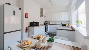 Eine moderne Küche mit weißen Schränken, einer Mikrowelle und einem Herd. Es gibt einen Esstisch mit Croissants und einer Pflanze.