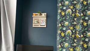 Ein Wohnzimmer mit dunkelblauer Wand, einem HolztV-Schrank, einem Flachbildfernseher, einer kleinen Holzablage mit Dekoration und einem gardine mit Blumendruck.