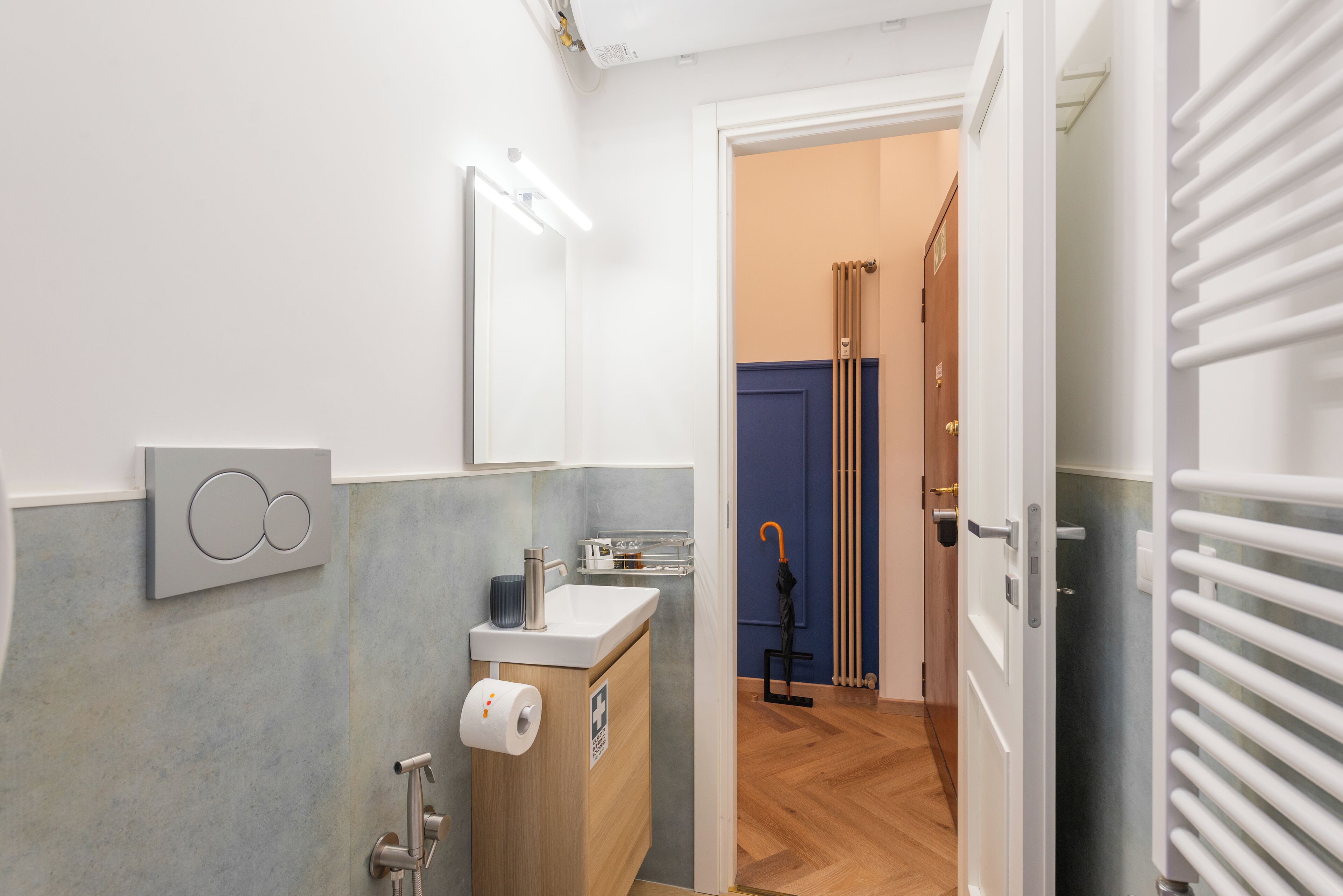 A modern bathroom with a toilet, sink, and mirror. There is a towel rack and a shower area visible.