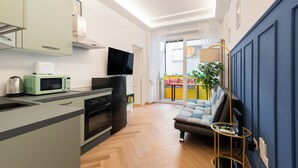 Een moderne keuken met een flatscreen televisie, een magnetron en een koelkast. In de woonkamer staat een bank en een kleine tafel met een lamp.