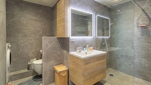 A modern bathroom with a wooden vanity, a large mirror, a shower enclosure, and a toilet.