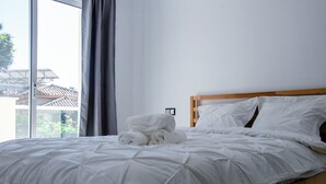 A neatly made bed with white linens and a wooden headboard in a room with large windows. - 6 bedroom villa with sea views (Mijas)