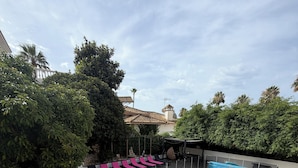 A swimming pool with a covered deck, surrounded by greenery and a tiled patio area.