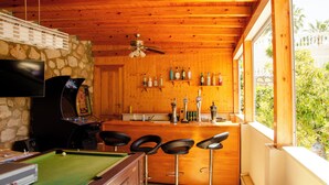 A pool table with four stools, a bar area with shelves of bottles, a television mounted on a stone wall, and a ceiling fan. - 6 bedroom villa with sea views (Mijas)