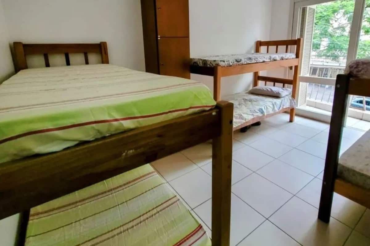 Ein Schlafraum im Studentenwohnheim-Stil mit Etagenbetten, einem Holzschrank und einem Balkon mit Blick.