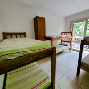 Une chambre de type dortoir, avec des lits superposés, une armoire en bois et un balcon offrant une vue.