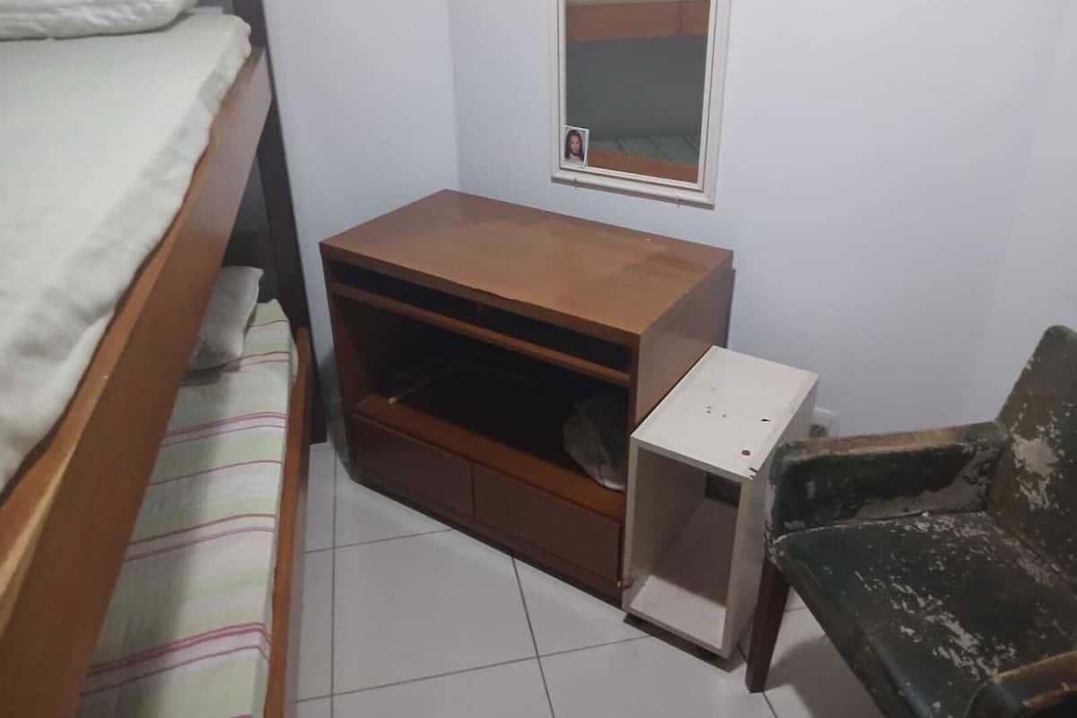 Ein Schlafzimmer mit einem Bett, einem Nachttisch aus Holz, einem kleinen Schreibtisch, einem Stuhl und einem Fenster mit Spiegel.