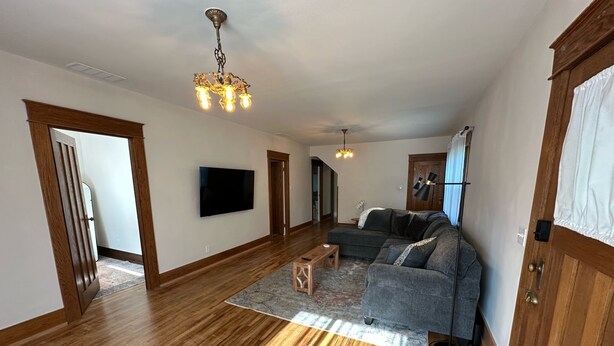 Un salón amplio con pisos de madera, un sofá modular, un televisor de pantalla plana y un candelabro.