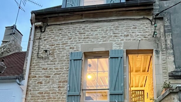 Een stenen gebouw met een trap die naar een tweede verdieping leidt. Er is een raam met luiken en een deur met een greep.