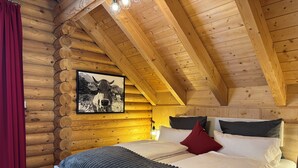Une chambre dans un chalet en rondins, avec un lit, des oreillers et un tableau encadré au mur.