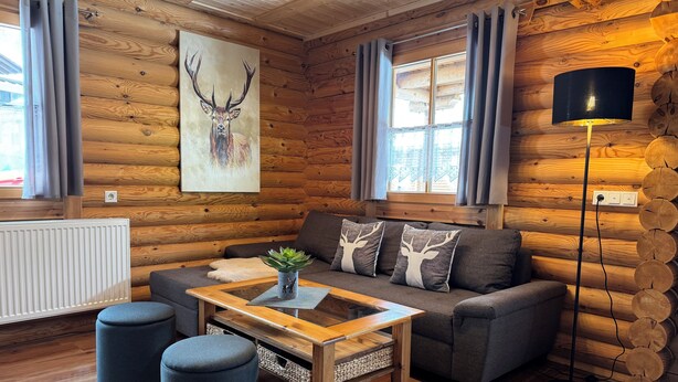 L’intérieur chaleureux d’un chalet en bois comprend un canapé, des poufs, une table basse et une lampe.